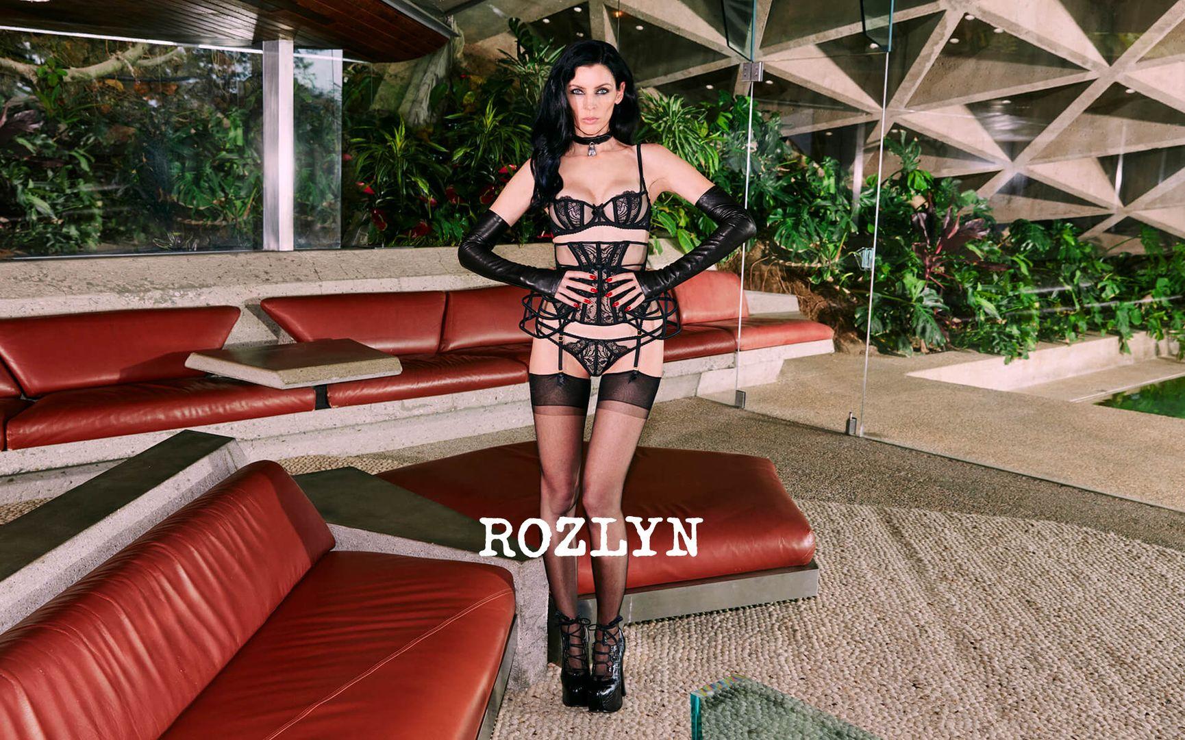 A brunette model poses with hands on hips, wearing the black Rozlyn lingerie set